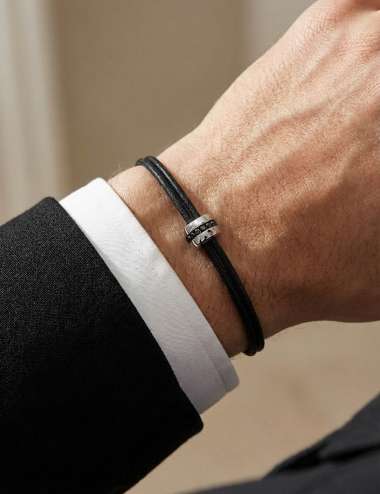 Bracelet homme D.Bachet en or blanc serti de diamants noirs sur cordon noir, porté au poignet.