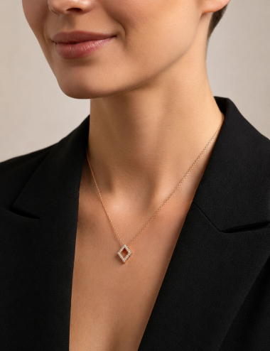 Pendentif losange ajouré en or rose et diamants blancs porté au cou d'une femme avec une veste noire.