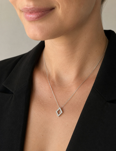 Openwork diamond-shaped pendant in white gold and white diamonds worn by a woman with a black blazer.
