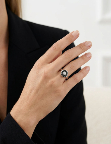Bague Allure en platine 950 avec diamant blanc central et entourage de diamants noirs, portée au doigt.