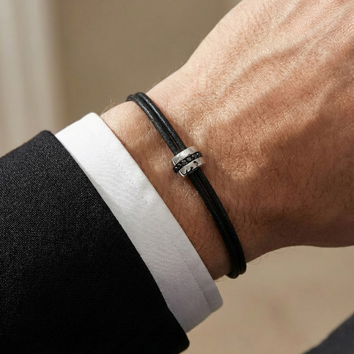 Bracelet homme cordon noir avec anneau en or blanc serti de diamants noirs porté au poignet avec un costume