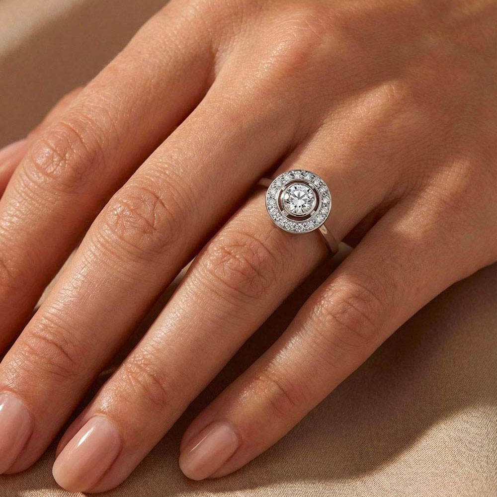 D.Bachet halo engagement ring worn with a 0.50-carat natural white diamond in a bezel setting and a halo of white diamonds.